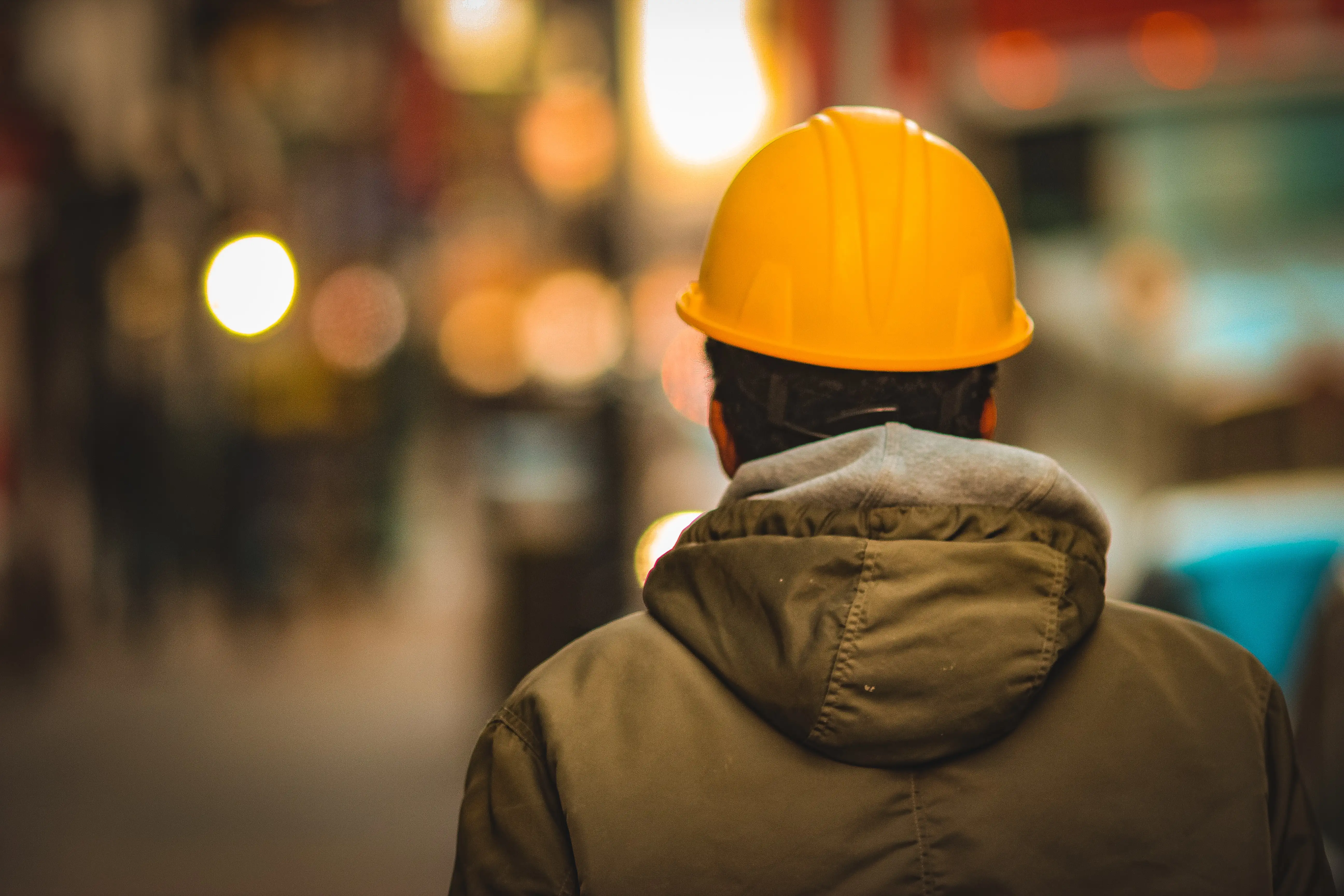 The backside of a worker with a yellow construction helmet and blurry background
